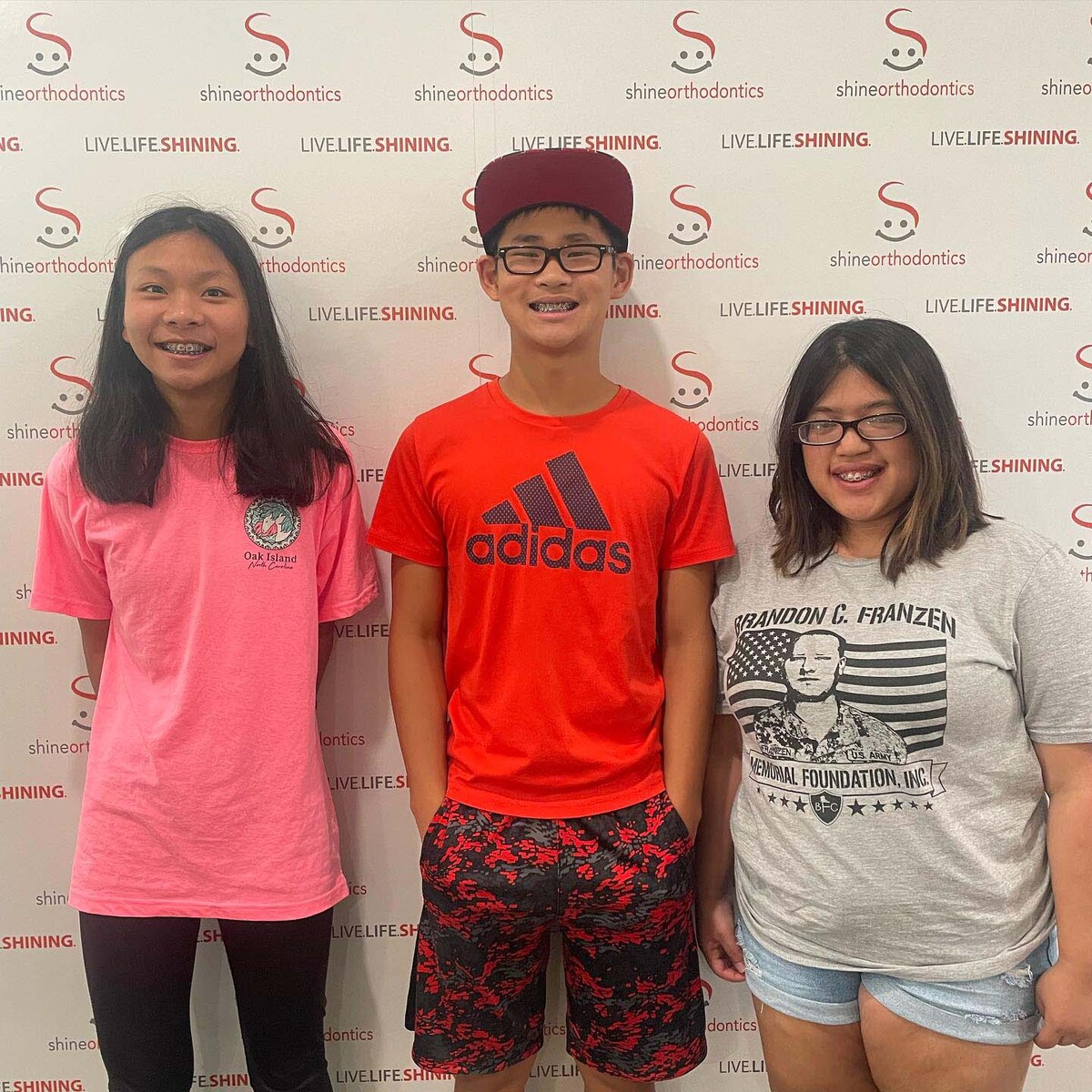 Three kids smiling in front of Shine Orthodontics backdrop